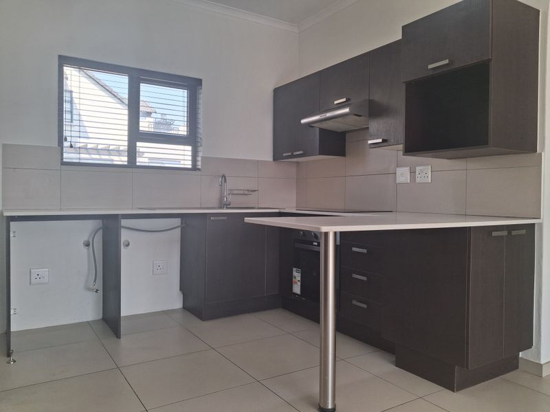 A modern kitchen featuring dark cabinetry, a breakfast bar, built-in oven, extractor fan, and tiled finishes, offering a clean and functional workspace.