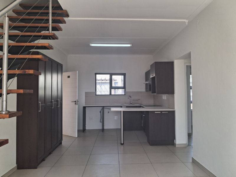Open plan living area featuring a modern staircase, tiled flooring, and a compact kitchen with built-in cabinetry and sink.