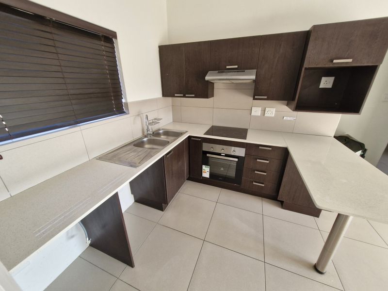 Modern kitchen featuring dark wood cabinetry, stone countertops, integrated electric hob and oven, stainless steel sink, and neutral tiled flooring.