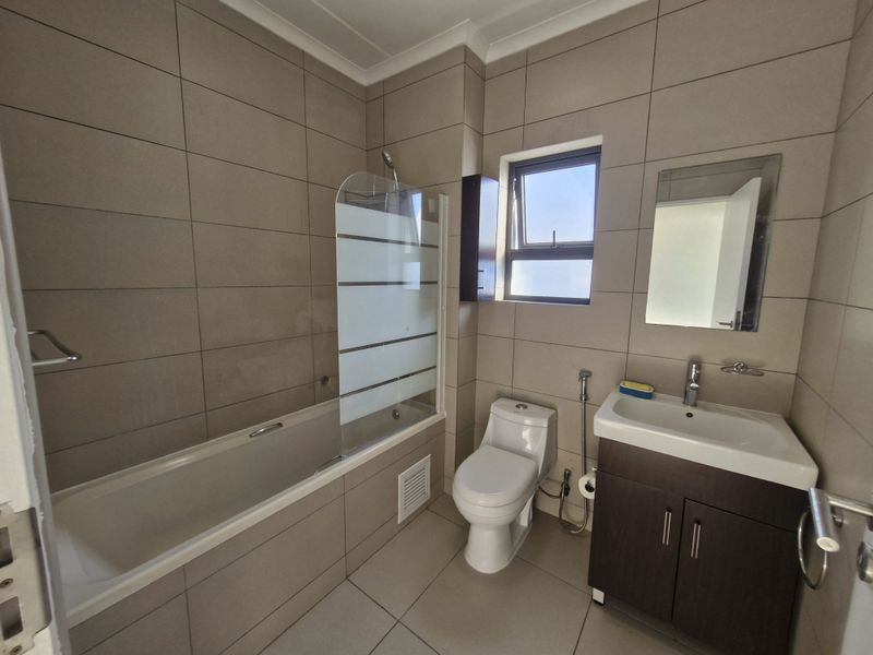A modern, well-maintained bathroom featuring neutral floor-to-ceiling tiling, a bathtub with a glass screen, a vanity unit with basin, and a toilet.