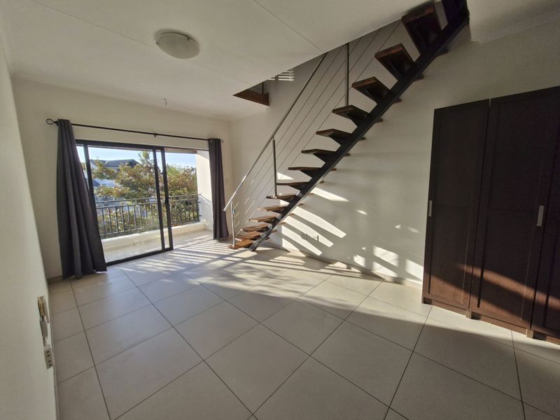 Spacious living area featuring tiled floors, an open-tread staircase with metal balustrade, and direct access to a private balcony through sliding glass doors.