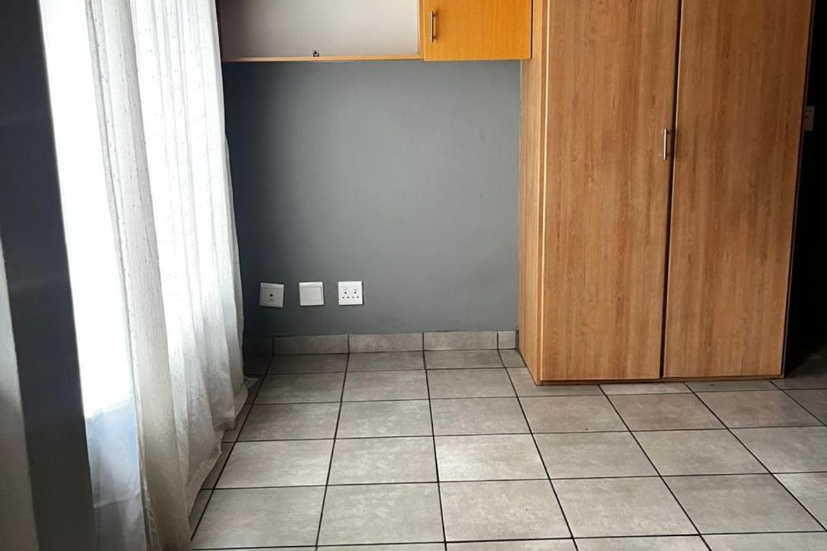 A clean, empty bedroom featuring neutral tiled flooring, a built-in wooden wardrobe, and integrated shelving units against a grey accent wall.