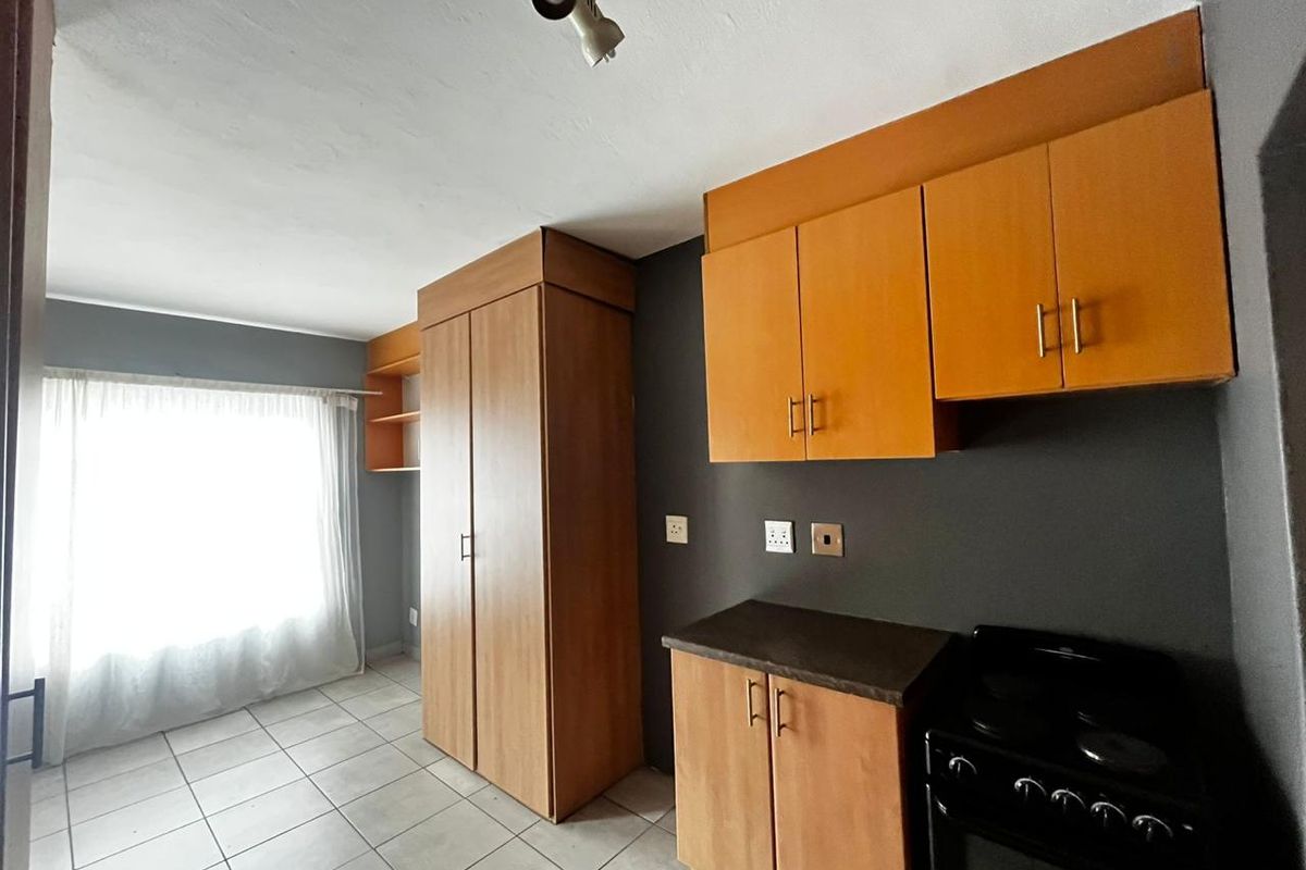 Compact kitchen featuring wood-look built-in cabinetry, laminate countertops, a freestanding stove, and tiled flooring in a neutral, open-plan layout.