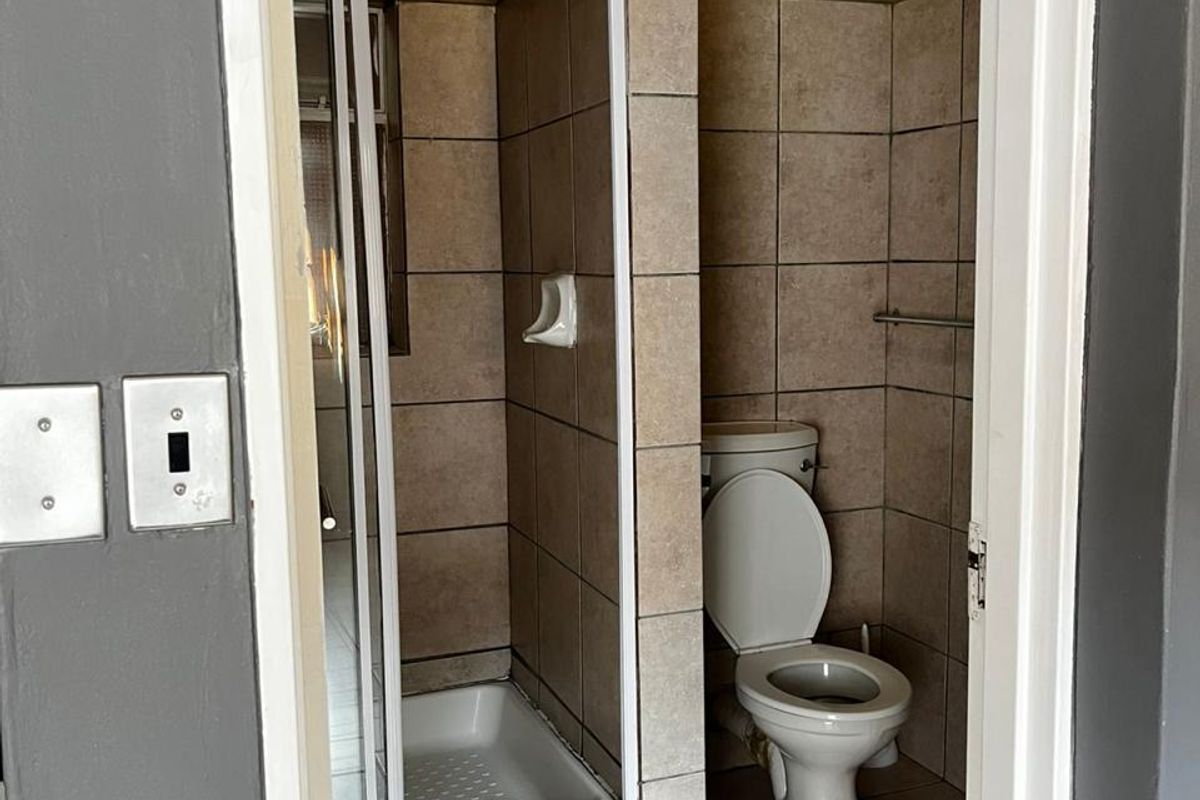 A functional bathroom featuring a shower enclosure, toilet, and neutral tiled finishes throughout.