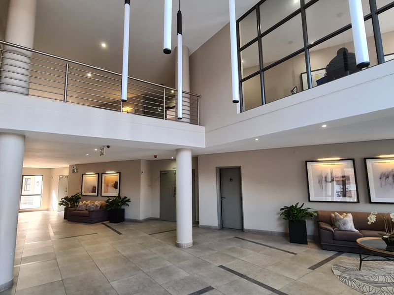 Spacious double-volume entrance lobby featuring tiled flooring, a mezzanine level with stainless steel balustrades, and modern pendant lighting.