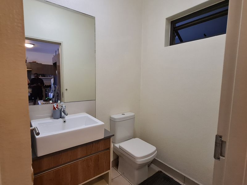A clean, functional bathroom featuring a modern vanity with a ceramic basin, a wall-mounted mirror, and a standard toilet.