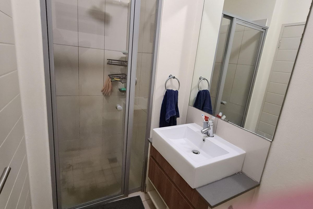 A compact bathroom featuring a modern vanity with basin, a wall-mounted mirror, and a glass-enclosed shower unit.