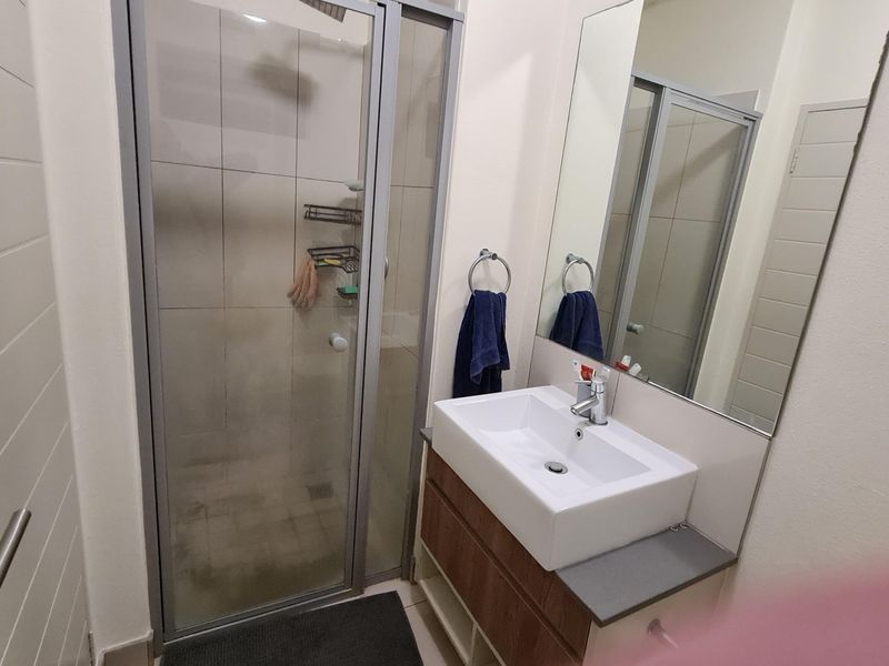 A compact bathroom featuring a modern vanity with basin, a wall-mounted mirror, and a glass-enclosed shower unit.