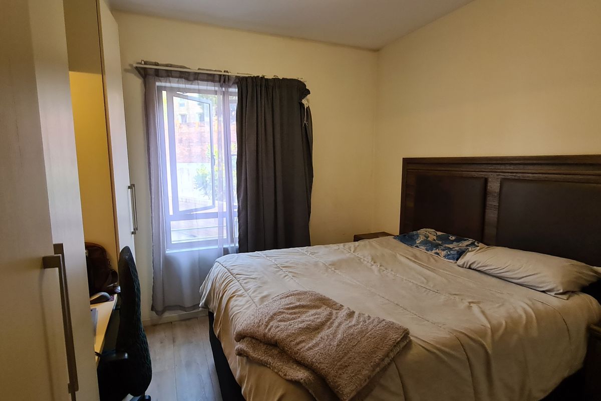 A functional bedroom featuring laminate flooring, a built-in wardrobe, and a window with curtains, providing a comfortable and practical living space.