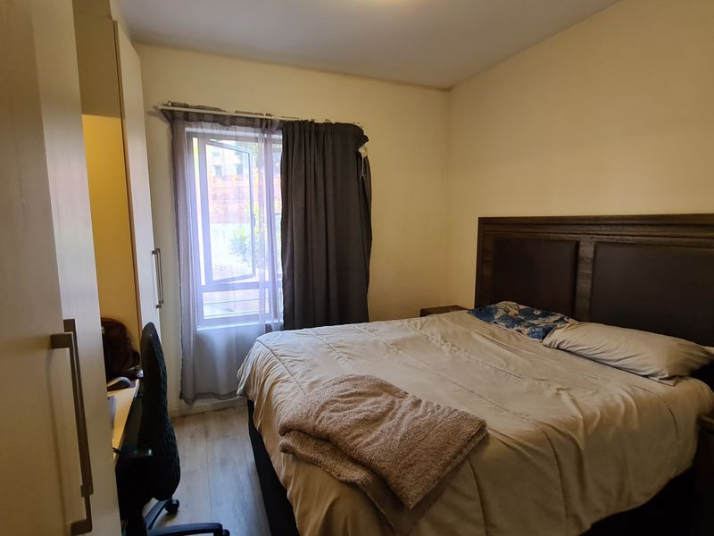 A functional bedroom featuring laminate flooring, a built-in wardrobe, and a window with curtains, providing a comfortable and practical living space.