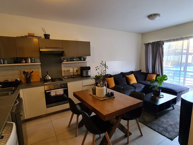 Open-plan living area featuring a compact kitchen with built-in cabinetry, gas hob, and oven, flowing into a lounge space with sliding door access.
