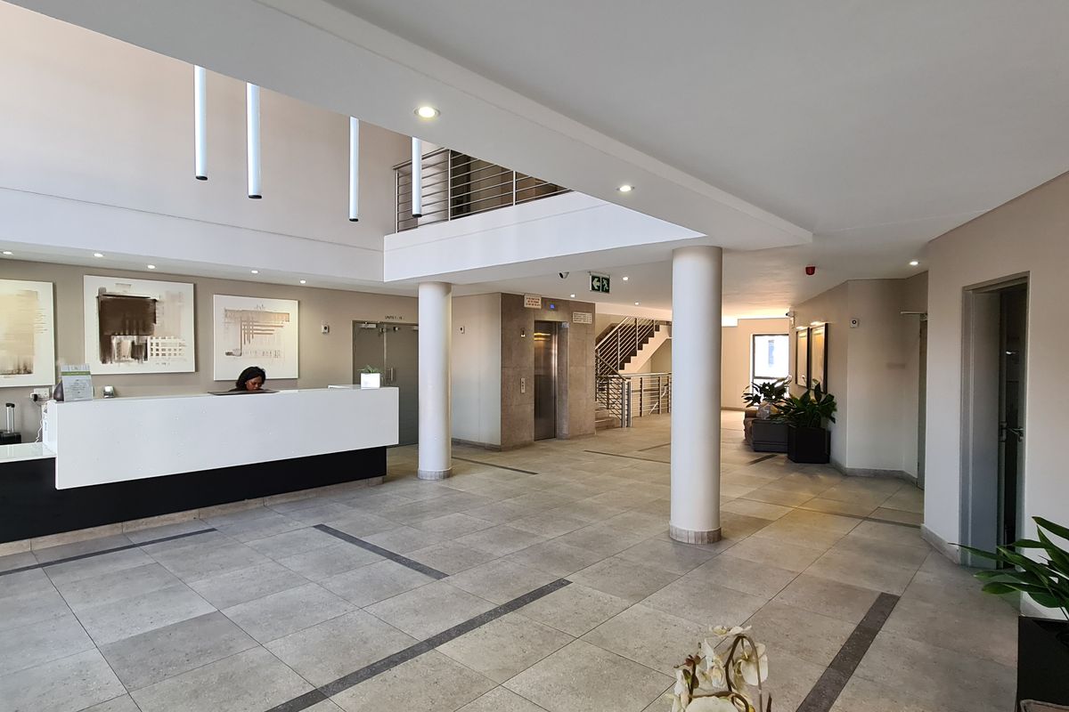 Spacious apartment building lobby featuring a reception desk, elevator access, tiled flooring, and a mezzanine level with a staircase.
