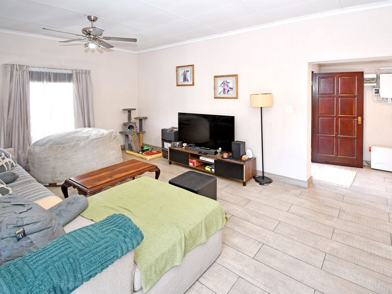 A comfortable living room featuring tiled flooring, a ceiling fan, and a solid timber panel door leading to an adjacent area.
