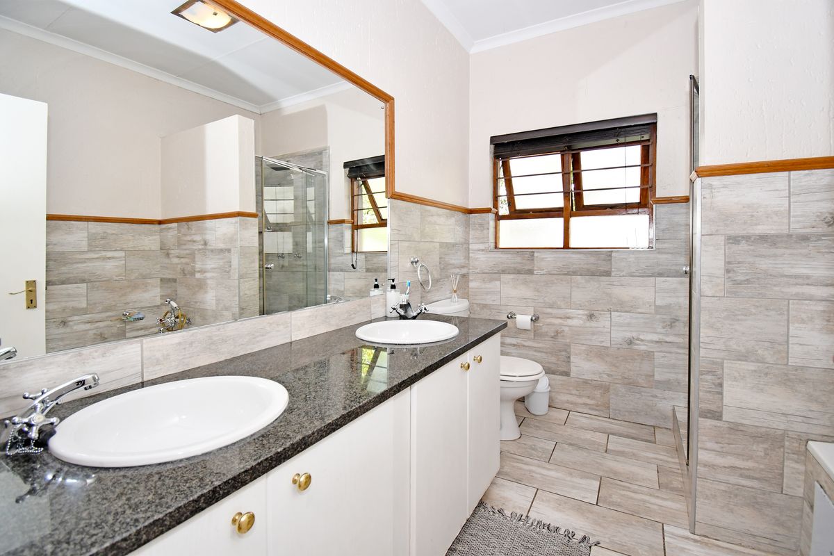 A well-maintained bathroom featuring a double vanity with granite countertops, large wall mirror, tiled finishes, and a separate shower enclosure.