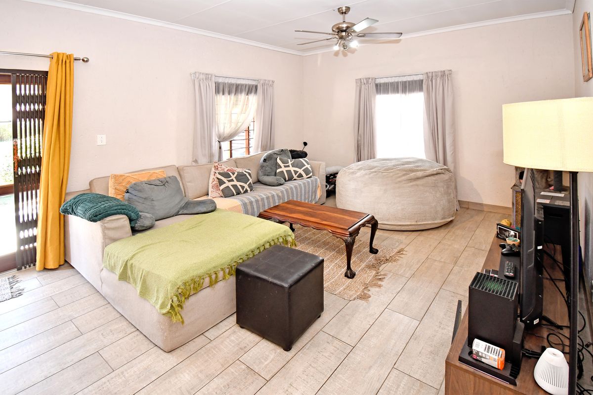 A living room featuring tiled flooring, a ceiling fan, and a sliding door with a security gate leading to the exterior.