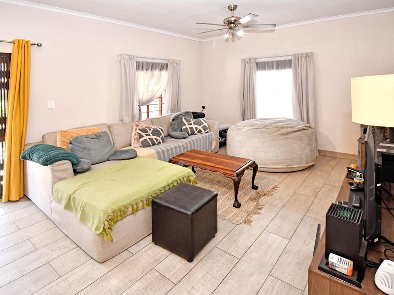 A living room featuring tiled flooring, a ceiling fan, and a sliding door with a security gate leading to the exterior.