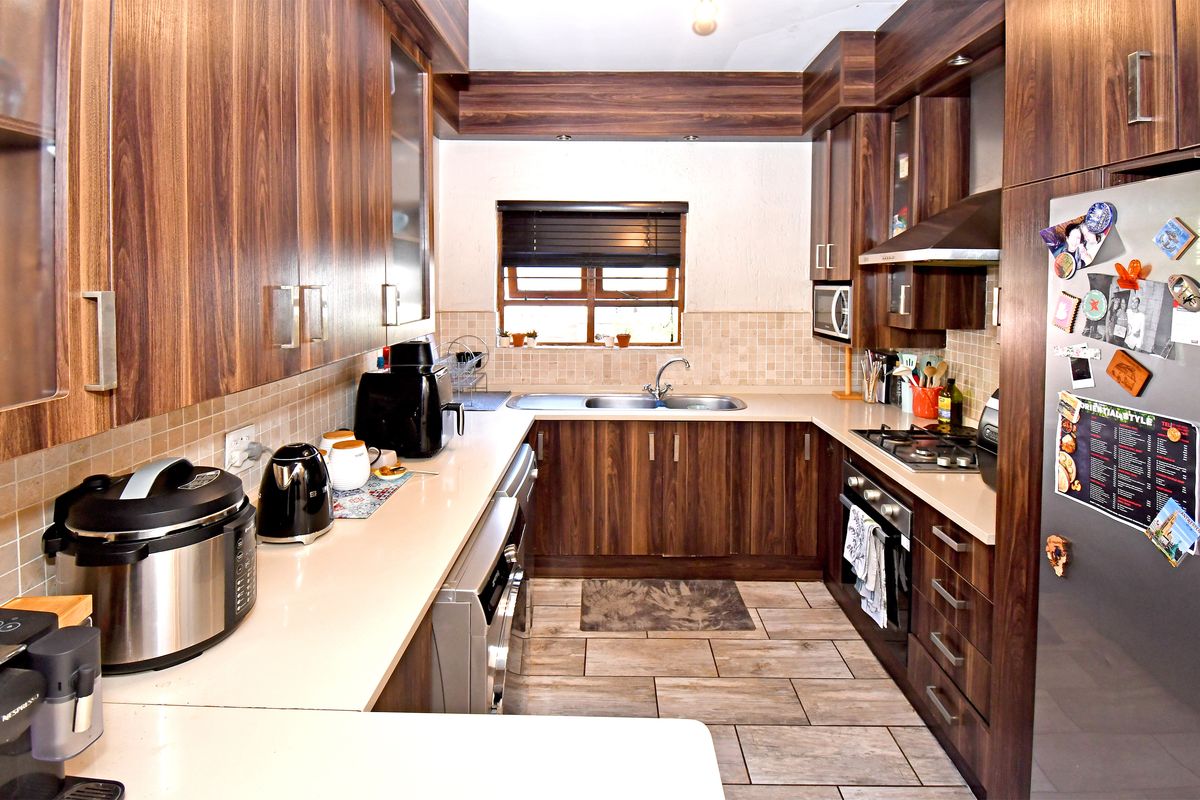 A functional galley-style kitchen featuring wood-grain cabinetry, stone-look countertops, a gas hob, and a double bowl stainless steel sink with tiled splashbacks.