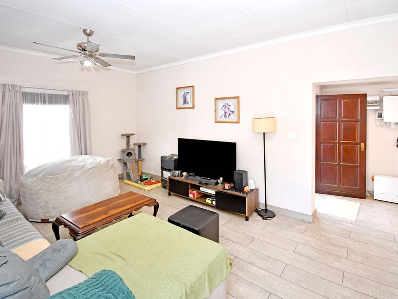 A living room featuring tiled flooring, a ceiling fan, and a solid wood door leading to an adjacent area with an installed inverter system.