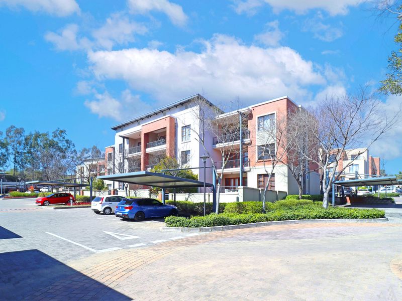 Exterior view of a modern apartment complex featuring brick facade, private balconies, and dedicated covered parking bays within a well-maintained residential estate.