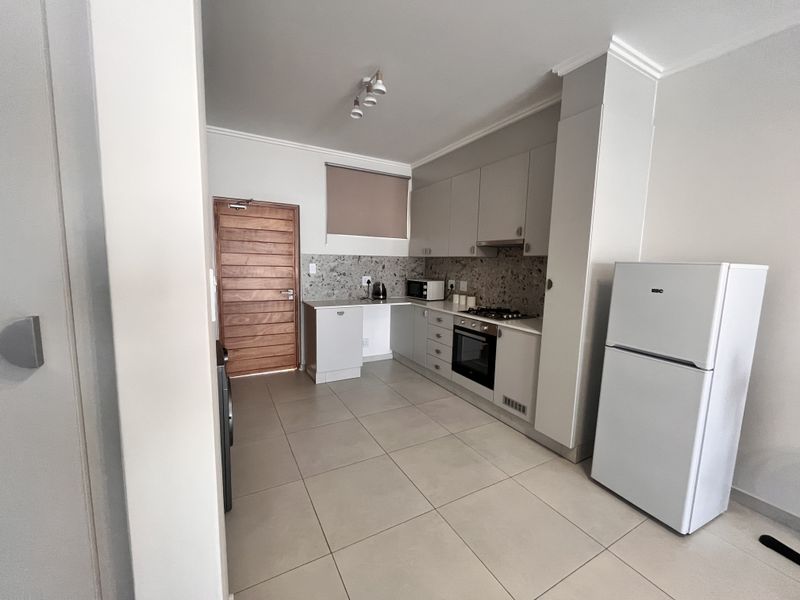 Modern kitchen featuring neutral cabinetry, stone-look backsplash, built-in oven, gas hob, extractor fan, and tiled flooring with direct access to an exterior door.