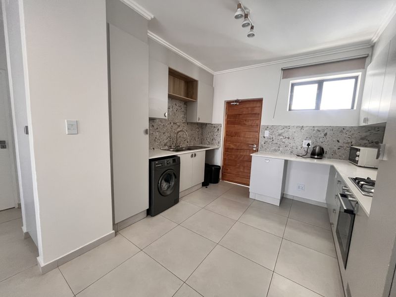 Modern kitchen featuring light grey cabinetry, terrazzo-style backsplash, tiled flooring, and integrated appliances, offering a clean and functional cooking space.