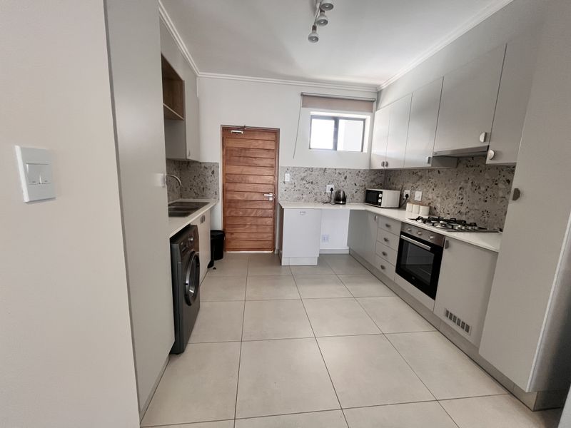Modern kitchen featuring light grey cabinetry, terrazzo-style backsplash, integrated oven, gas hob, and tiled flooring with a dedicated laundry appliance space.