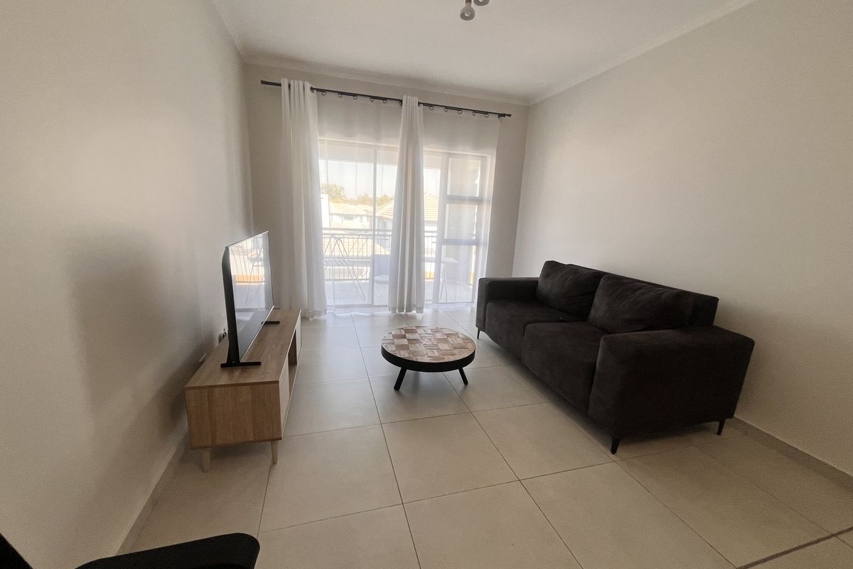 A bright living room featuring large format floor tiles and a sliding glass door providing access to an outdoor balcony area.