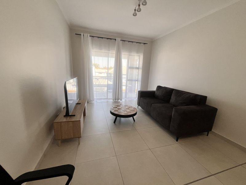 A bright living room featuring large format floor tiles and a sliding glass door providing access to an outdoor balcony area.