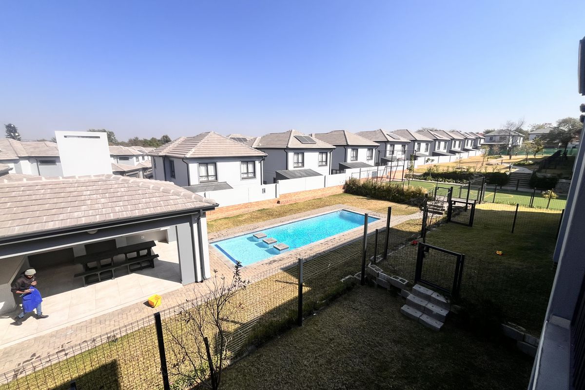 An elevated view of a residential property featuring a swimming pool, a covered patio area, and a well-maintained garden within a secure estate.