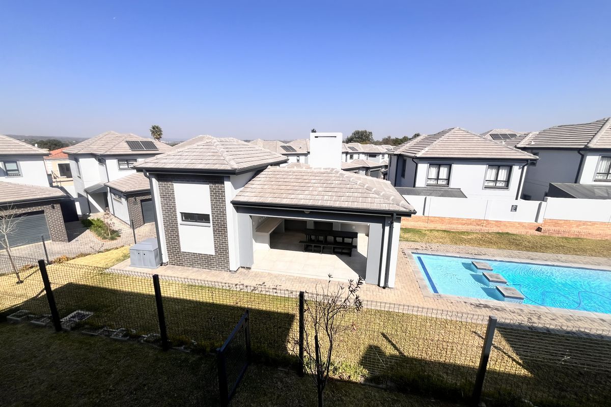 Rear view of the property featuring a covered patio with built-in braai, a swimming pool, and landscaped garden area within a secure complex.