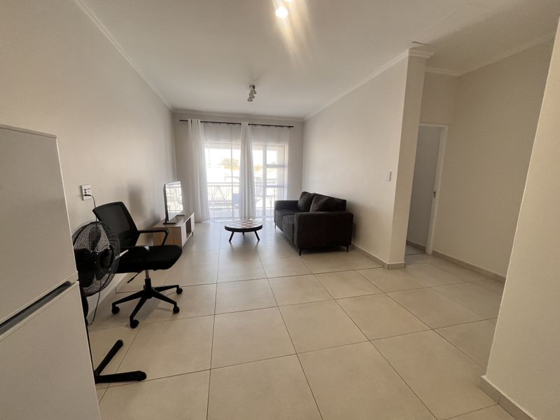A bright, open-plan living area featuring neutral tiled flooring and a sliding glass door providing access to an outdoor balcony.