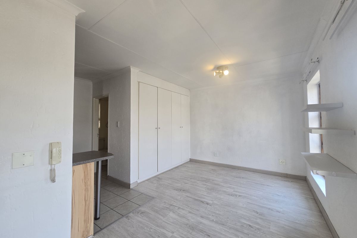 A bright, empty bedroom featuring light-toned laminate flooring, built-in cupboards, and floating wall shelves, offering a clean and versatile living space.