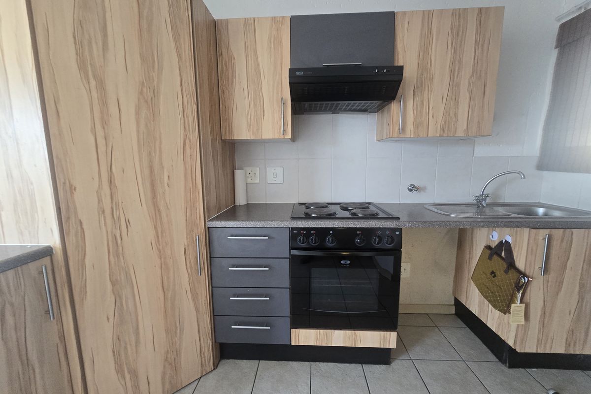A functional kitchen featuring wood-look cabinetry, dark grey accents, a built-in oven with hob, extractor fan, and tiled flooring.
