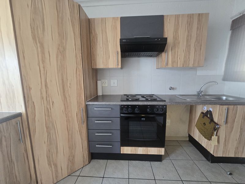 A functional kitchen featuring wood-look cabinetry, dark grey accents, a built-in oven with hob, extractor fan, and tiled flooring.