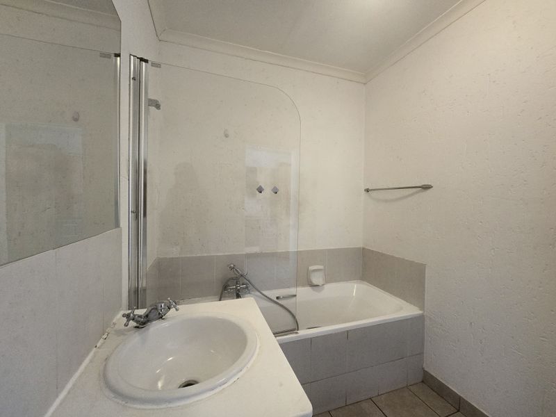 A functional bathroom featuring a built-in bathtub with a glass shower screen, a vanity basin, and neutral wall finishes.