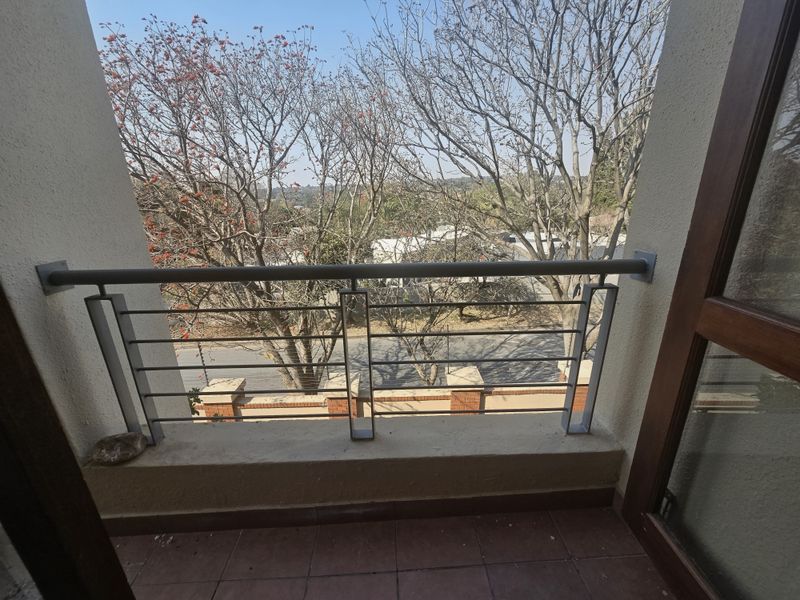 A compact balcony featuring a metal balustrade and tiled flooring, offering an elevated view of the surrounding trees and street.