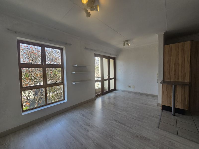 Bright open-plan living area featuring laminate flooring, built-in cabinetry with a breakfast counter, and access to a balcony through sliding glass doors.