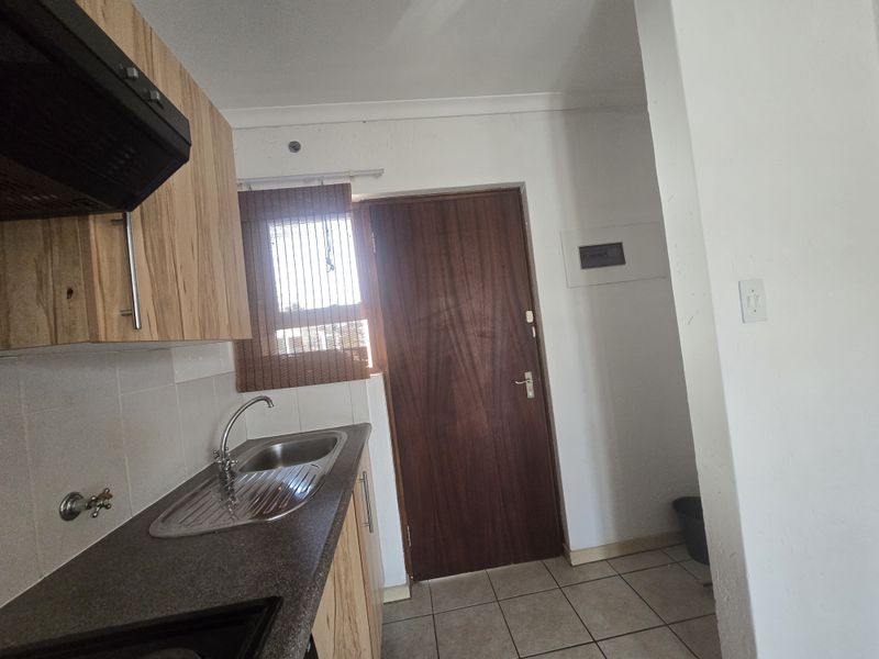 A functional kitchen area featuring laminate cabinetry, a stainless steel sink, tiled splashbacks, and an extractor fan, with direct access to an adjacent space.