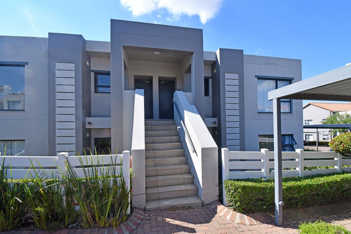 Front elevation of a modern apartment complex featuring a central staircase, paved walkway, and covered carport parking area.