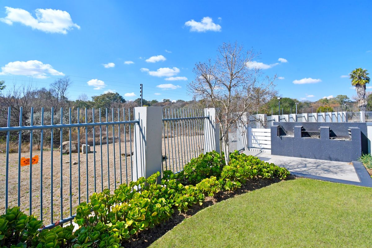 A well-maintained rear garden area featuring a built-in braai, paved patio, and secure steel palisade fencing with electric security wires.