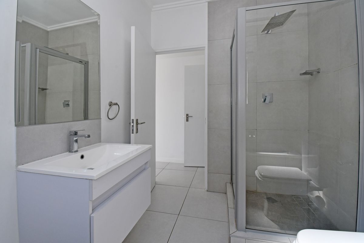 Modern bathroom featuring a sleek vanity cabinet, large wall mirror, and a glass-enclosed shower with contemporary tiling throughout.