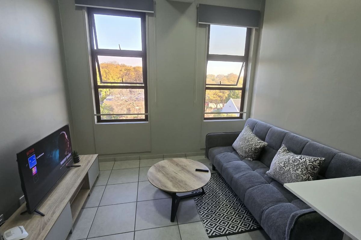 A bright living room featuring tiled flooring and dual windows with roller blinds, offering a functional and well-lit space.