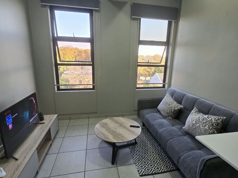 A bright living room featuring tiled flooring and dual windows with roller blinds, offering a functional and well-lit space.