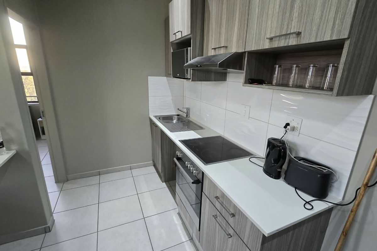 A modern, compact kitchen featuring wood-grain cabinetry, a built-in oven, electric hob, extractor fan, and clean tiled finishes.