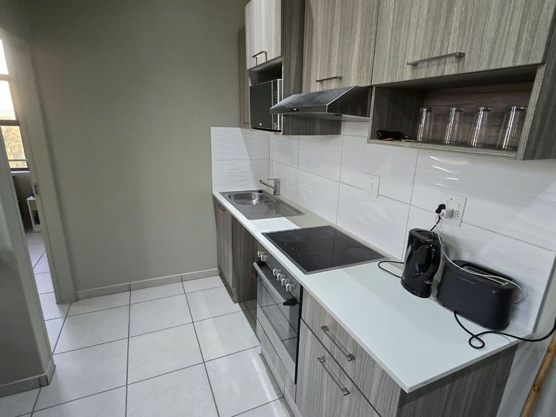A modern, compact kitchen featuring wood-grain cabinetry, a built-in oven, electric hob, extractor fan, and clean tiled finishes.