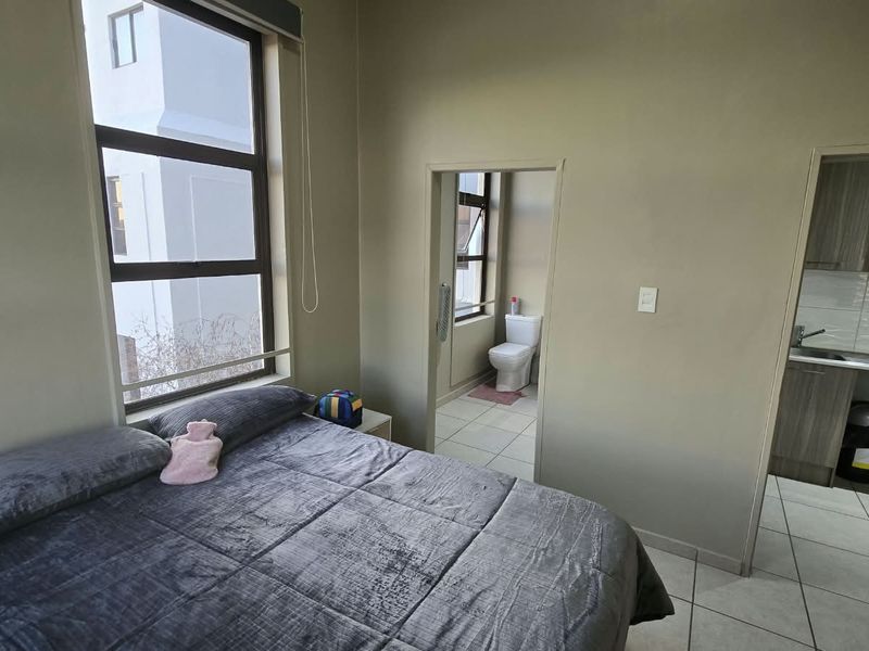 A bedroom featuring large windows, tiled flooring, and direct access to an en-suite bathroom and adjacent kitchen area.