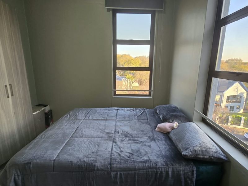A functional bedroom featuring built-in wardrobes, large aluminium-framed windows providing natural light, and neutral wall finishes.