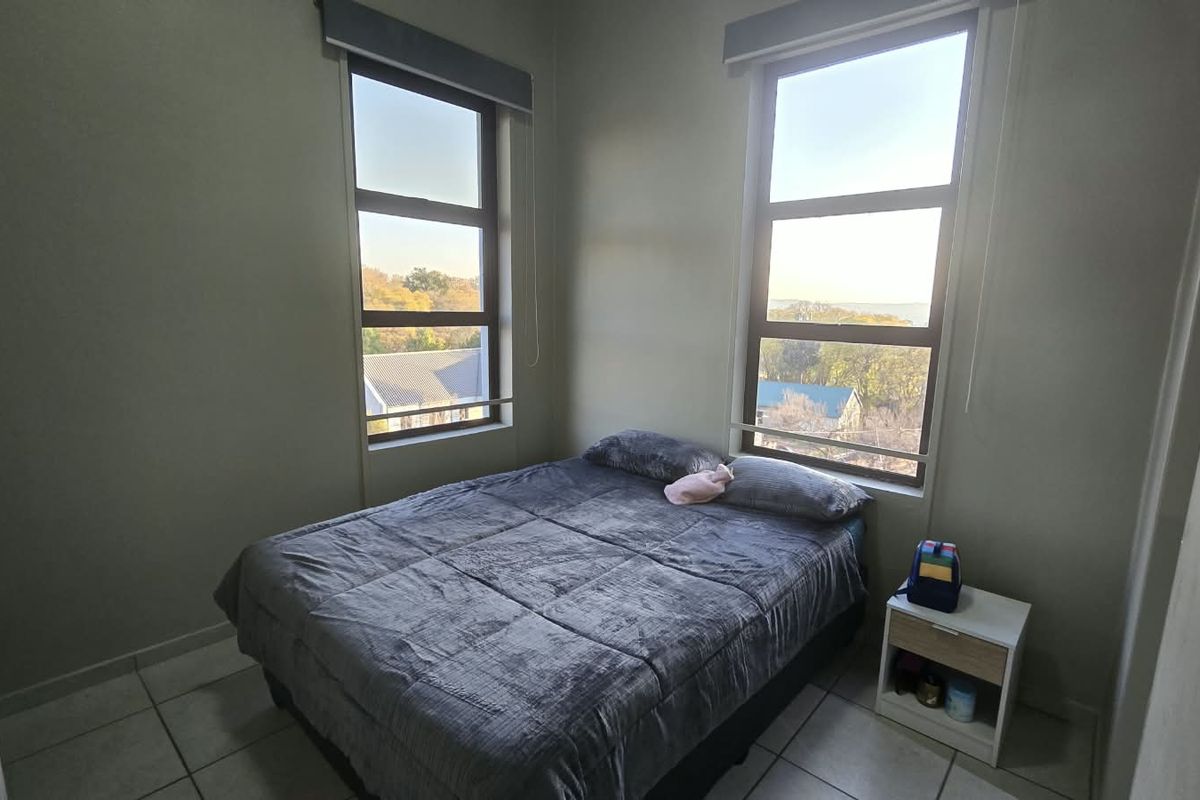 A bright bedroom featuring tiled flooring, built-in cupboards, and large windows that provide natural light and exterior views.