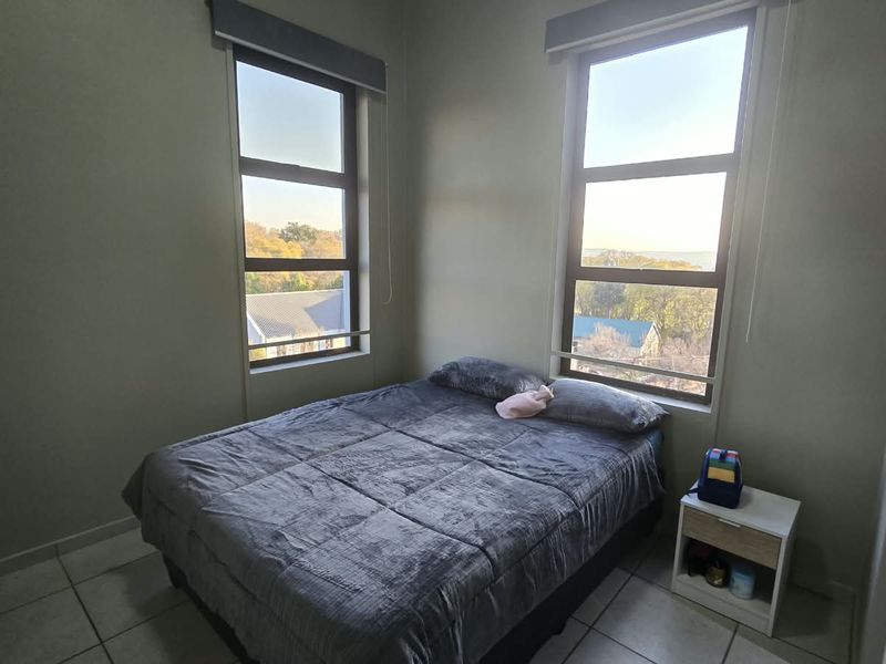 A bright bedroom featuring tiled flooring, built-in cupboards, and large windows that provide natural light and exterior views.