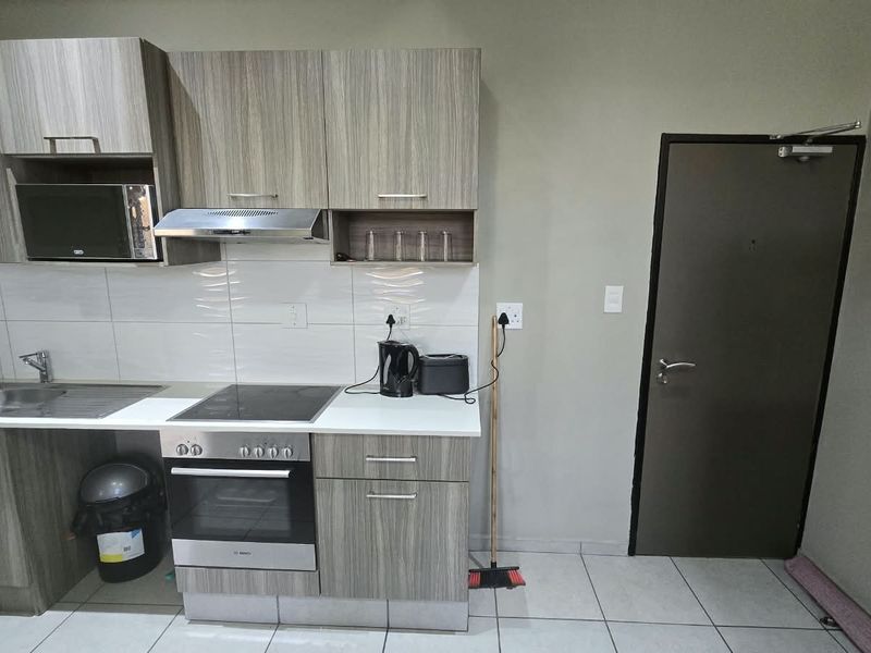 A functional kitchen featuring modern wood-grain cabinetry, integrated stainless steel appliances, a tiled backsplash, and durable floor tiles.